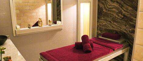 A spa room with a massage table, a mirror, and a marble wall.