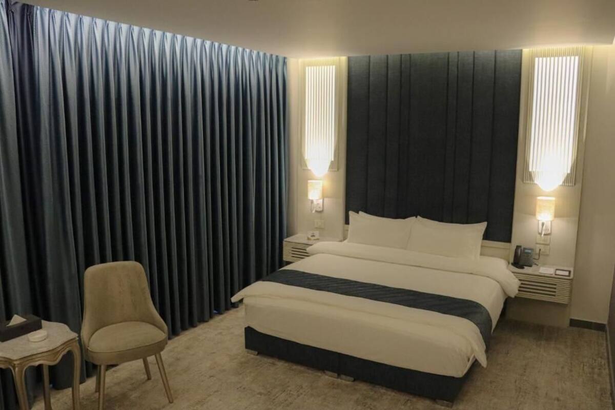 Una camera d'albergo con un letto grande, due comodini con lampade, una sedia e una tenda.