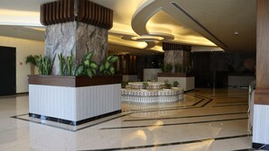 Un vestíbulo espacioso con suelo de mármol, grandes columnas decorativas y una zona de estar central con baldosas estampadas.