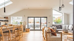 A spacious living area with a kitchen, wooden furniture, and large windows. - Little Beach House by Bloom Stays -  a holiday let that sleeps 8 guests  in 3 bedrooms (Whitstable)