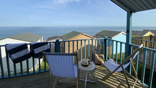 A covered deck with a view of the sea, two striped beach chairs, a hat, and a small table. - Little Beach House by Bloom Stays -  a holiday let that sleeps 8 guests  in 3 bedrooms (Whitstable)