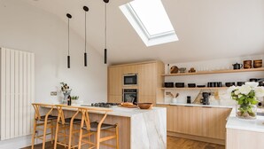 A modern kitchen with a central island, wooden bar stools, a skylight, and wooden cabinets. - Little Beach House by Bloom Stays -  a holiday let that sleeps 8 guests  in 3 bedrooms (Whitstable)