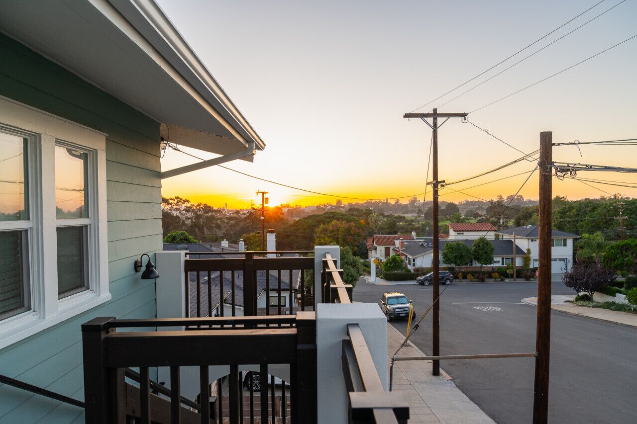 Una calle residencial con casas, un coche aparcado y un atardecer al fondo.