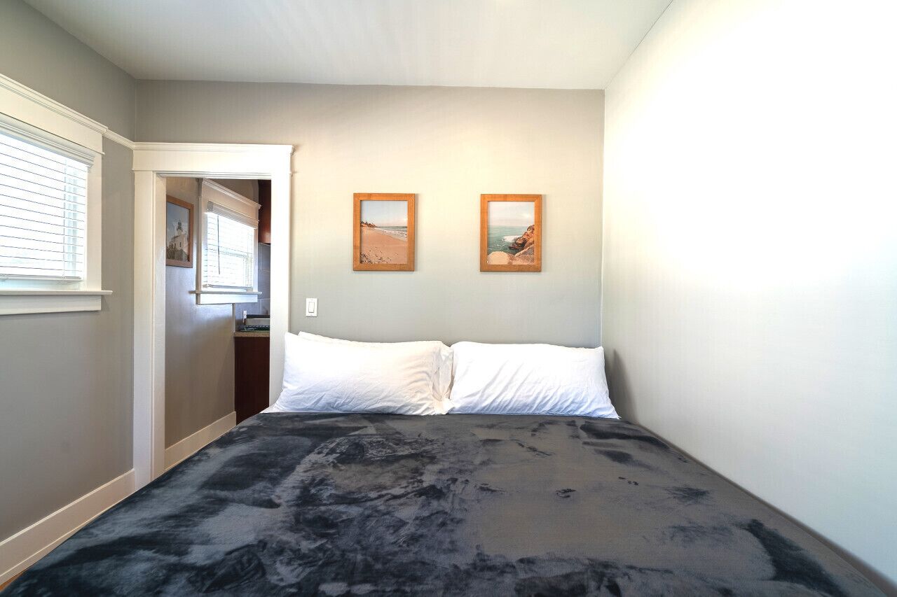 A bedroom with a bed, two framed pictures on the wall, and a window with blinds.