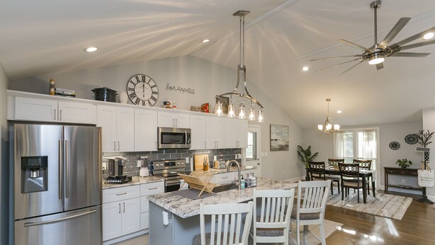 Een moderne keuken met roestvrijstalen apparatuur, een centraal eiland met barkrukken, en een eethoek met houten stoelen.