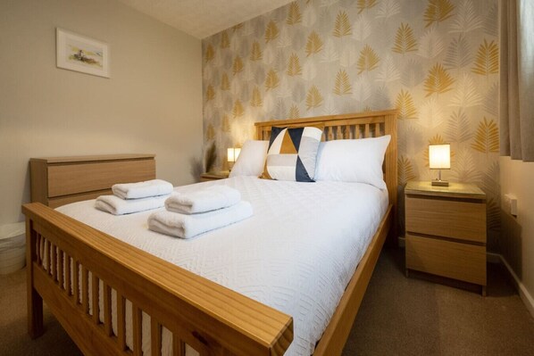 A neatly made bed with white linens and towels, a wooden headboard, and a nightstand with a lamp. - Number 4 in Central Fort William (Fort William)