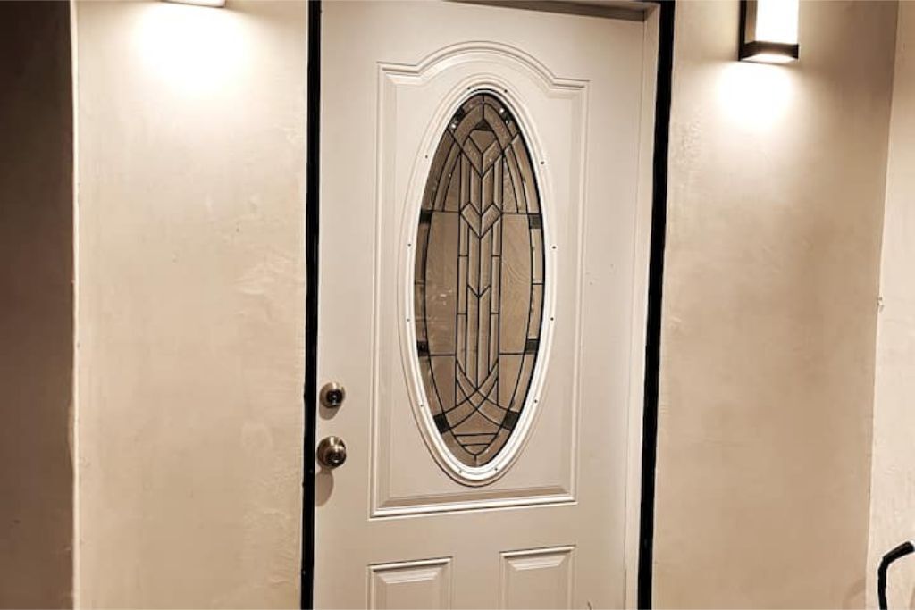 Une porte blanche ornée d’un panneau de verre décoratif et de deux petits panneaux situés en dessous.