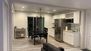 A modern kitchen with white cabinets, a stainless steel refrigerator, and a microwave. There is a dining area with a black table and chairs, and a black leather sofa in the foreground. - New Private house in historic area- Pasadena (Pasadena)