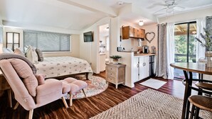 Una habitación compacta con cama, una silla, escritorio y kitchenette.