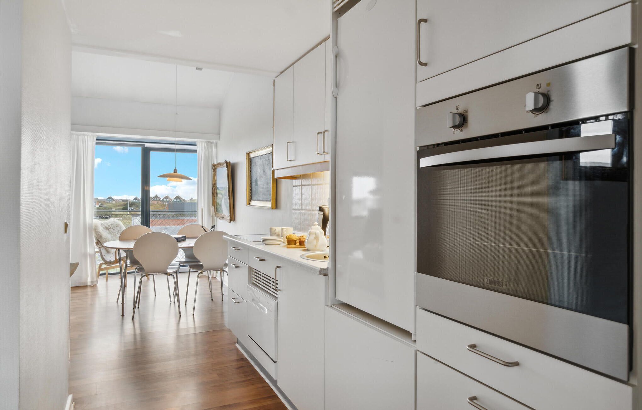 A modern kitchen with stainless steel appliances, white cabinetry, and a dining area with a view.