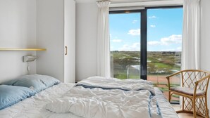 A bedroom with a bed, a chair, a wardrobe, and a window with a view of a landscape. - 1 bedroom beach front apartment in Fanø (Fanø)