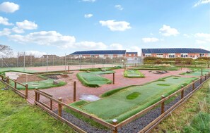 A miniature golf course with a brick pathway, green grass, and a wooden fence.