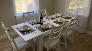 Ett matbord dukat för fyra personer, med vita stolar, en vinflaska och tallrikar.