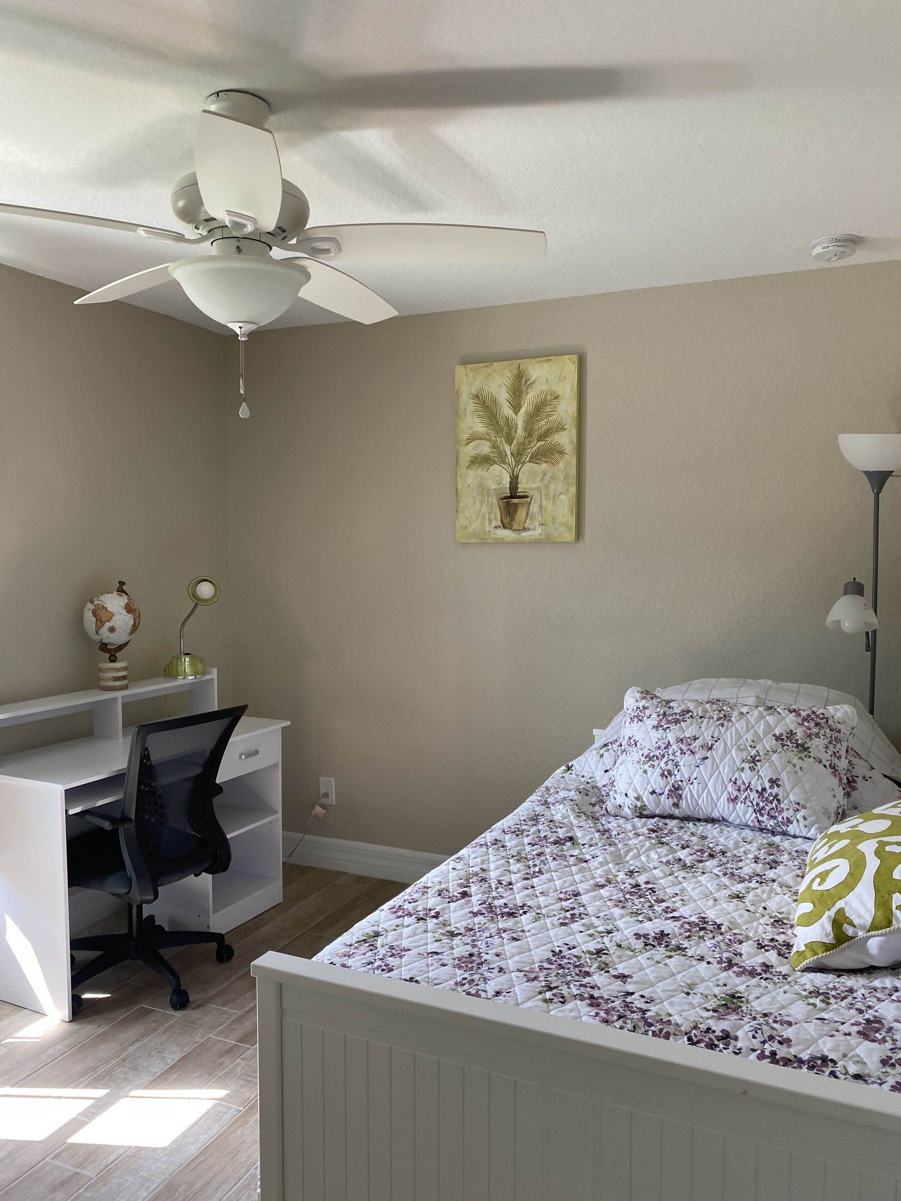 Een slaapkamer met een bed, bureau, stoel, plafondventilator en een wereldbol aan de muur.