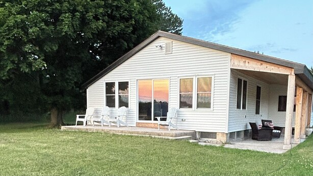 Ein Bungalow mit überdachter Veranda, großen Fenstern und Sitzgelegenheiten im Freien.