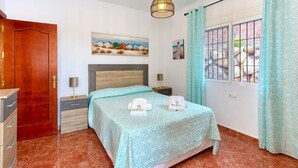 Un dormitorio con cama, mesita de noche, cómoda, un cuadro y ventana con cortinas.