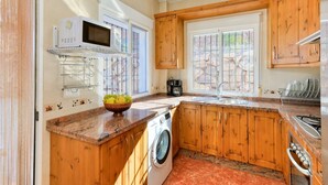 Una cocina funcional con armarios de madera, lavadora integrada, microondas y un lavamanos.
