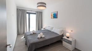 Una habitación de hotel moderna con dos camas, un ventanal con cortinas, una mesita de noche con lámpara y un cuadro en la pared.