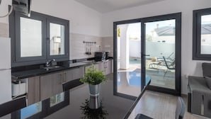 Una cocina moderna con una isla central, un área de comedor con separador de vidrio y vistas a una piscina y zona de estar exterior.