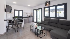 Una sala de estar moderna con un sofá gris, una mesa de centro de vidrio y una cocina con un comedor.