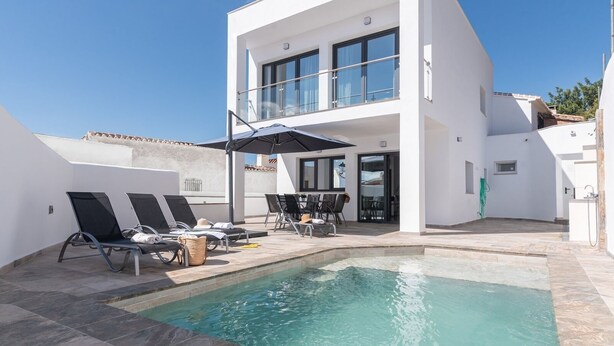 Un edificio moderno de dos pisos con piscina, mobiliario exterior y un patio cubierto.