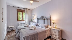 A bedroom with two beds, a nightstand with a lamp, a window with curtains, and a radiator.