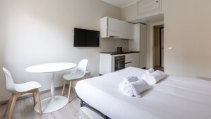 Una camera d'albergo con un letto, un angolo cottura, un tavolo rotondo con sedie e una TV a parete.