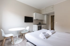 Habitación de hotel con cama, una kitchenette pequeña, una mesa redonda con sillas y un televisor montado en la pared.