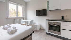 Una camera d'albergo moderna con un letto, un tavolino, una sedia, una televisione e un angolo cottura.