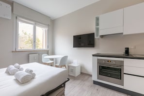 Una habitación de hotel moderna con cama, una mesita, una silla, televisión y kitchenette.