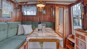 A cozy cabin interior with a wooden interior, a sofa, a table with glasses, and a hanging light fixture. - Historic Charming Boat in Downtown Harbor

 (Gig Harbor)