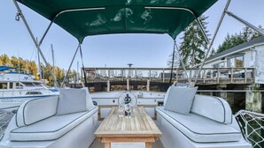 A boat deck with two white cushioned seating areas, a wooden table, and a green canopy. - Historic Charming Boat in Downtown Harbor

 (Gig Harbor)