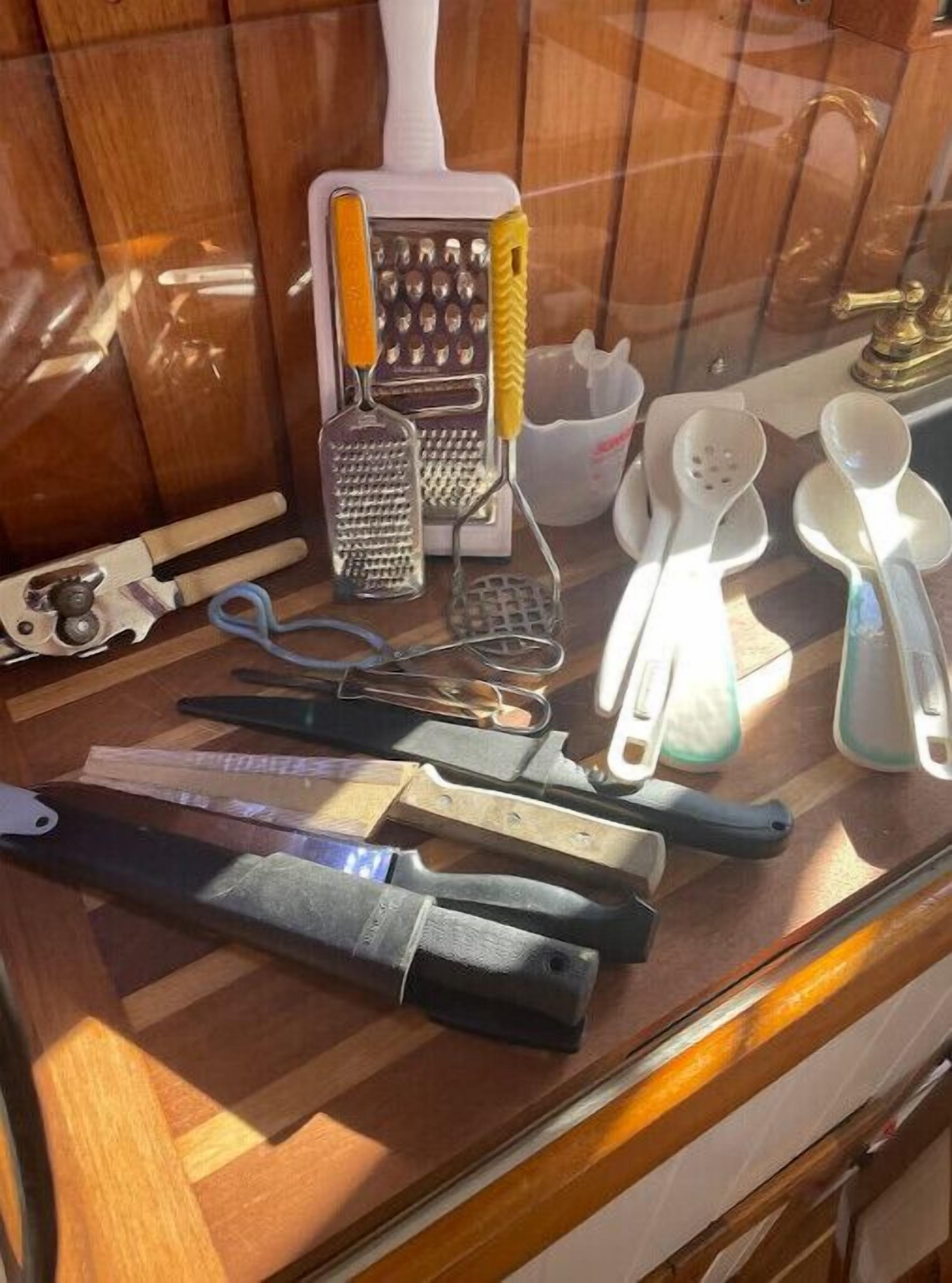 A kitchen counter with various utensils, including a grater, a pair of tongs, and a knife.