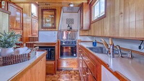 A compact kitchen with wooden cabinets, a built-in oven, and a sink. - Spacious 46' Yacht: Luxury, kayaks, walk to town

 (Gig Harbor)
