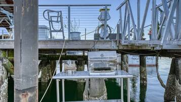 A metal dock structure with a grill and a chair, surrounded by water and wooden posts.