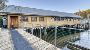 Un muelle de madera que lleva a un edificio con techo metálico, ubicado sobre el agua.