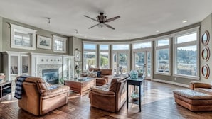 A spacious living room with leather sofas, a fireplace, and large windows offering a view of the city. - Waterfront high end home-dock, hot tub fun

 (Gig Harbor)