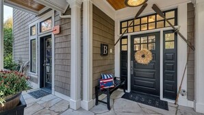 A house entrance with a black door, a bench with a flag cushion, and a wreath on the door. - Waterfront high end home-dock, hot tub fun

 (Gig Harbor)