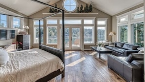 A spacious bedroom with a large bed, a sitting area with a sofa, and a view of the outdoors through large windows. - Waterfront high end home-dock, hot tub fun

 (Gig Harbor)