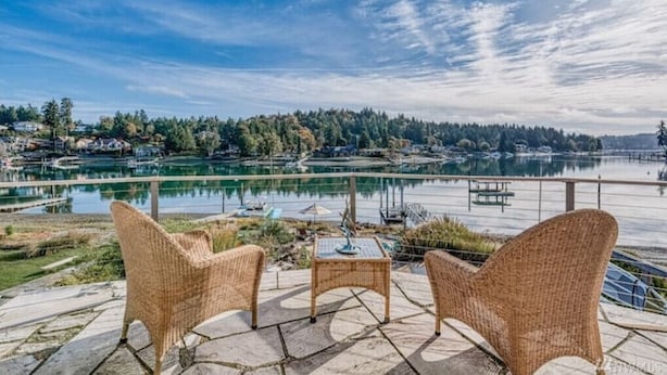 A patio with wicker furniture overlooking a lake with boats, surrounded by trees and houses. - Waterfront high end home-dock, hot tub fun

 (Gig Harbor)