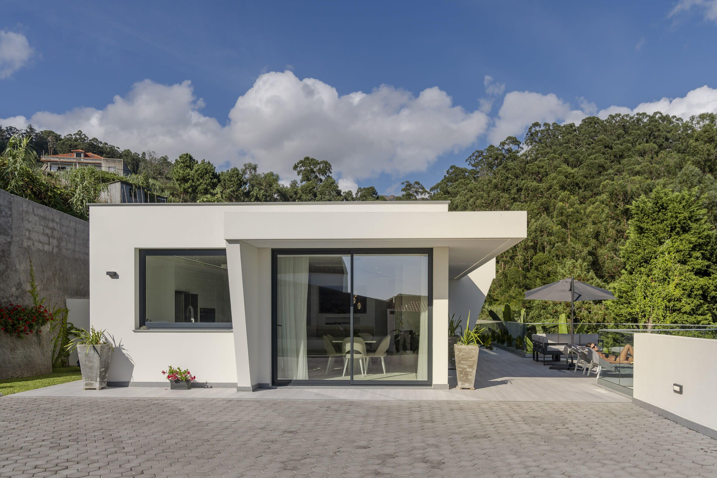 Une maison moderne dotée d’un patio, de grandes portes-fenêtres coulissantes et offrant une vue sur une colline verdoyante.