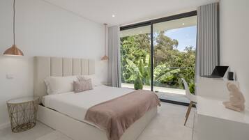 Une chambre moderne avec un grand lit, une table de chevet, une lampe et une vue sur la verdure grâce à une porte-fenêtre coulissante.