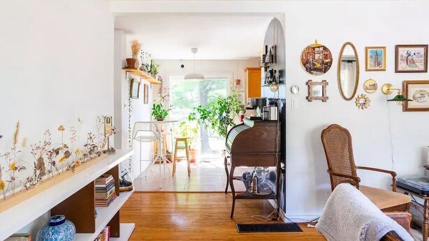 Un salon chaleureux avec un plancher en bois, un piano, un fauteuil en osier et une bibliothèque remplie de livres et d’objets décoratifs.