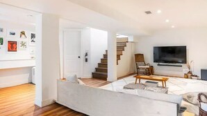 Un salon moderne avec un canapé, une table basse et un téléviseur. Un escalier mène à un niveau supérieur.