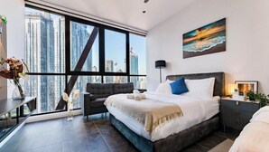 A modern bedroom with a large bed, a desk, and a view of tall buildings. - Scarletz Suites KLCC by M SUITES (Kuala Lumpur)