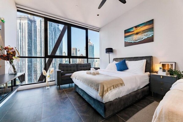 Een moderne slaapkamer met een groot bed, een bureau en uitzicht op hoge gebouwen.