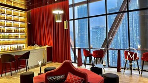 Een moderne hotellobby met een rode fluwelen gordijn, een bar met flessen en een groot raam met uitzicht op de stad.