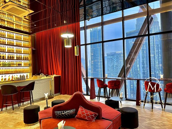 A modern hotel lobby with a red velvet curtain, a bar area with bottles, and a large window offering a city view. - Scarletz Suites KLCC by M SUITES (Kuala Lumpur)