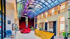 Een ruime lobby met een hoge plafond, een receptiebalie, rode zitplaatsen en een glazen atrium.