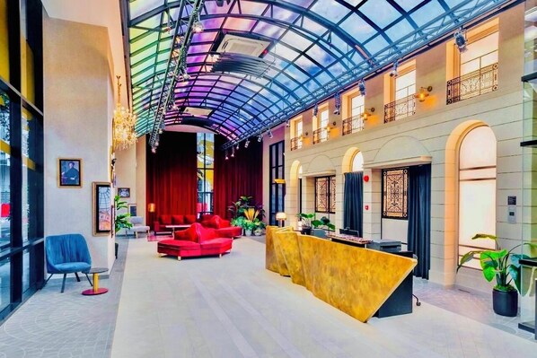 Un hall d’entrée spacieux avec un plafond haut, un comptoir d’accueil, des sièges rouges et un atrium en verre.